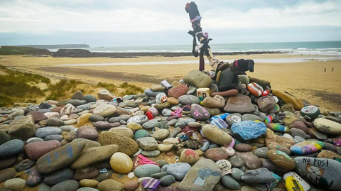 Pentwr o gerrig crynion gyda lluniau a negeseuon wedi eu paentio arnyn nhw ar draeth Freshwater West ger Penfro