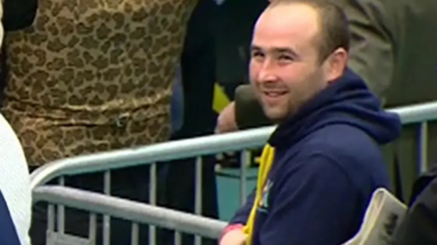 Thomas O'Hara has very short black hair and is smiling. He is wearing a blue hoodie and standing among a group of people.