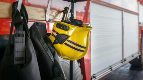 Firefighting equipment on hooks attached to a fire engine. A yellow fire helmet can be seen in the image.
