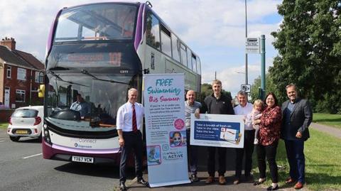 Transport bosses in front of a double-decker bus and a sign promoting free swimming for under-16s