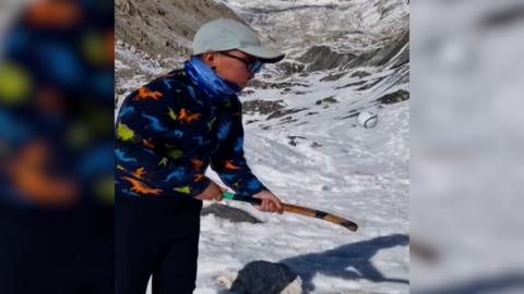 A young boy does keepy-ups with a shinty stick and ball on the slopes of Mount Everest.