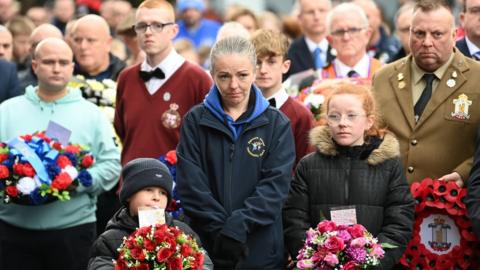 Two children hold bouquets of flowers with a large crowd of people behind them