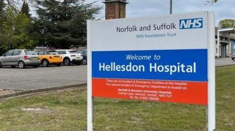 Hospital sign for Hellesdon Hospital, with parked cars and buildings in the background.