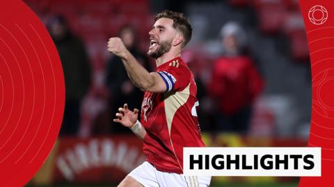 Luke Garbutt celebrates with fist in the air in red Salford City kit