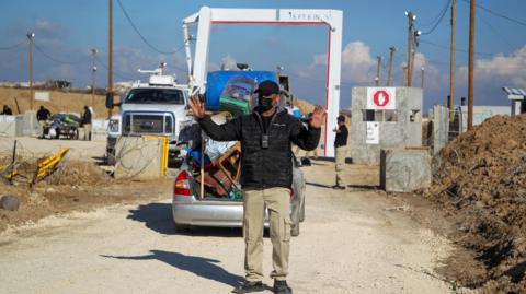 A member of the Egyptian-Qatari committee gestures while inspecting vehicles carrying displaced Palestinians at a screening area south of Gaza City (27 January 2025)