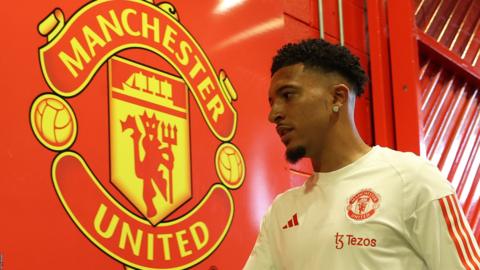 Jadon Sancho walks past the Manchester United badge