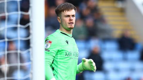 Murphy Cooper wearing a green goalkeeper kit of Sheffield Wednesday standing in the goal during a match