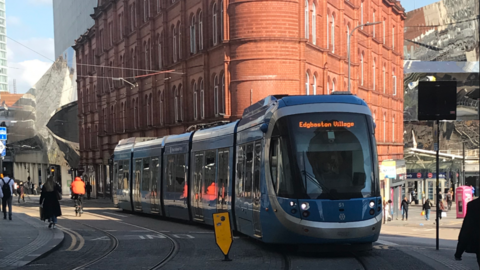 A blue tram on the lines in central Birmingham with a brick building in the background