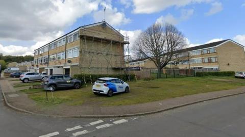 A housing estate with scaffolding on the side of the building. Four cars can be seen on driveways. 