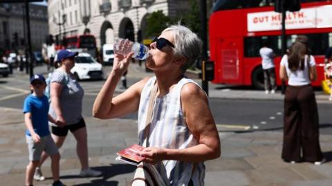A woman finishes a water bottle as pedestrians are seen behind her