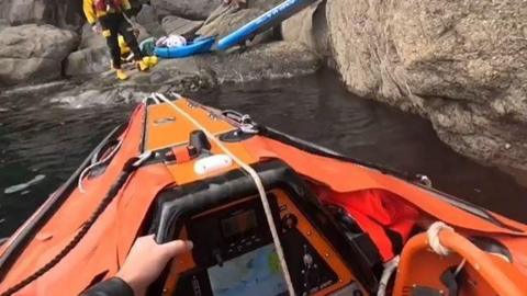 A view from the rescue lifeboat showing crew members assisting Mr Bascombe on rocks