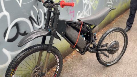 An illegal e-bike leaning against the wall of an underpass, covered in graffiti
