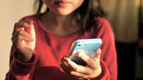 A stock image of a young child holding a pale blue smartphone