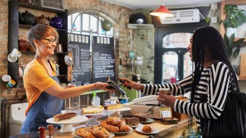 Woman in coffee shop paying for a cup of coffee and cake with her mobile phone.