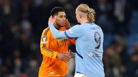 Jude Bellingham covers his mouth talking to Erling Haaland who is about to hug him