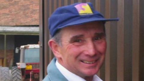 Rocky Poulson stood in front of a tractor wearing a blue hat 