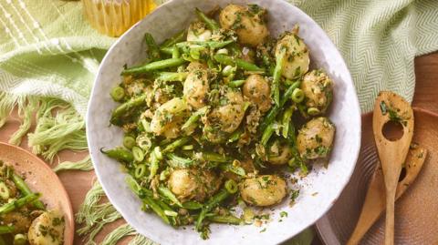 A white bowl of herby potato salad with green beans and sliced spring onions