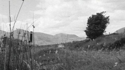 A car driving around the Irish countryside with some mountains in the background