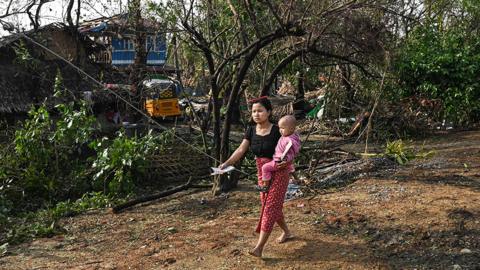Woman carries baby as she walks past ruins of her village in Myanmar after Cyclone Mocha