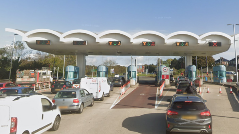 A queue of vehicles waiting to go through a series of toll lanes on a bridge.