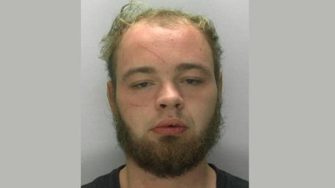 A police mugshot of Ben Tregartha. He has a scruffy light ginger beard and thinning brown hair