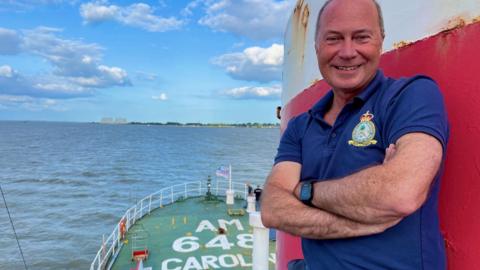 A smiling man wearing a purple shirt on the boat.