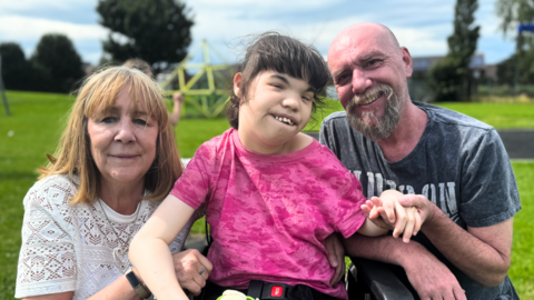 Parents sit with their daughter who is in a wheelchair.