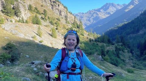 Geraldine McFaul poses in front of hills with her hiking gear.