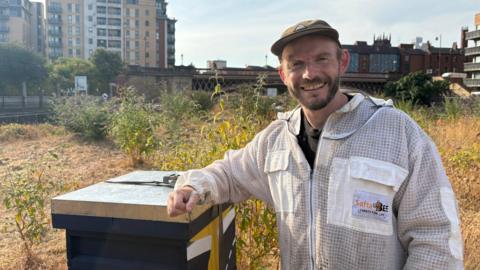 Tom is an urban beekeeper standing beside his beehive at Leeds Dock