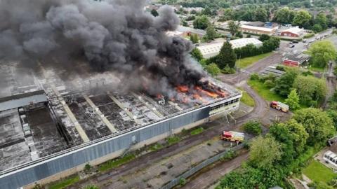 Aerial view of the fire at the former Delphi Diesel Systems site, showing thick black smoke pouring into the air while firefighters try to hose the site down.