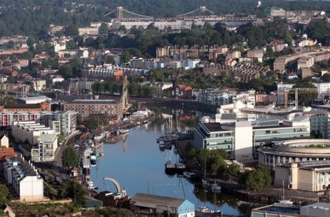 An aerial view of the centre of Bristol with the floating harbour in the foreground and the Clifton Suspension Bridge in the distance