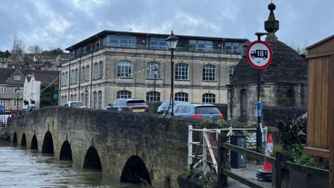 St Margaret's Hall in Bradford-on-Avon. In the foreground is a bridge with cars going over it. The Avon is quite high.