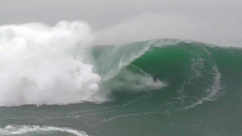 A wide shot of a surfer riding the tube of a large wave as it curls and breaks