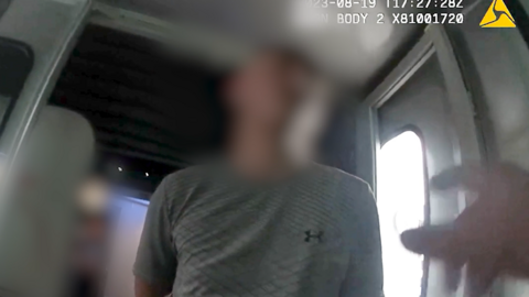 Police body-camera footage of Callum Coady, 27, whose face has been blurred by police, standing in front of the camera in the entrance to an aeroplane. He is wearing a grey Under Armour branded t-shirt. 