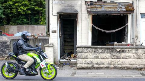 A motorist drives his motorcycle past a damaged house, after a second night of an anti-immigration demonstration in Ballymena, Northern Ireland, on June 11, 2025.