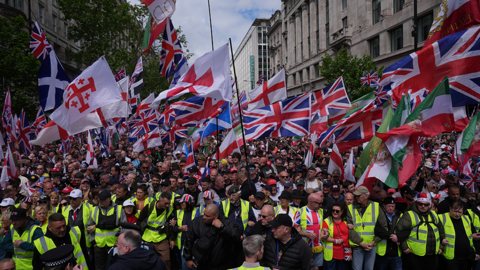 Thousands of people waving flags, with a front row in high-vis jackets
