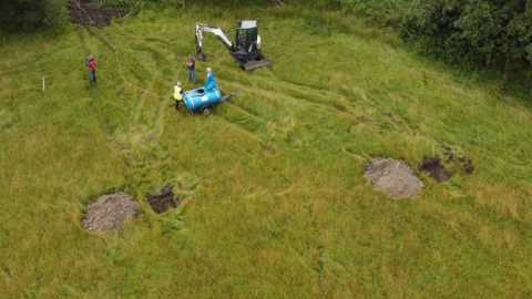 Work machinery and people stand in a grassy field - the site that will become the new base for the Duddon and Furness Mountain Rescue Team. 