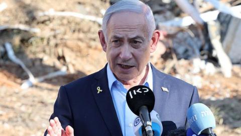 Benjamin Netanyahu gives a statement during a visit to the site of the Weizmann Institute of Science, which was hit by an Iranian missile barrage. He wears a light blue shirt and navy blazer. 