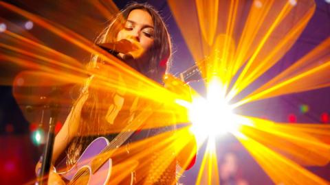 Olivia Rodrigo performing on stage with a dazzling orange stage light behind her