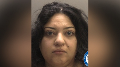 A mugshot of a woman with dark hair in a centre parting. She has a nose ring.