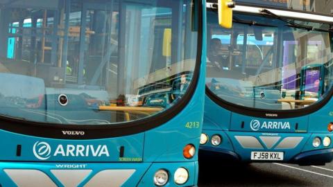 Two blue Arriva buses parked next to each other in parking bays. The buses are empty except for their drivers and have large windscreens.