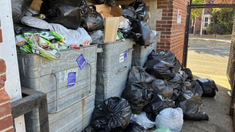 black bags of rubbish piled high outside blocks of flats