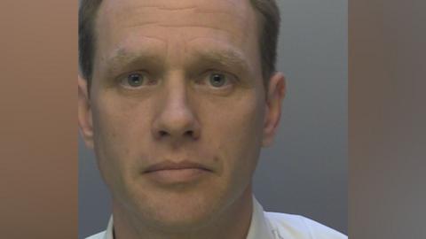 A mugshot of Joel Hanby issued by police. He is wearing a white shirt and looking at the camera.