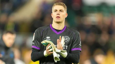 Goalkeeper Paul Nardi holding his gloves in his hands and clapping while walking on the pitch at the end of a QPR match