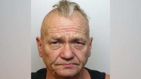 Thomas Brewer. He has a shaved head and a small amount of hair down the middle. He is pictured against a white background and is frowning.