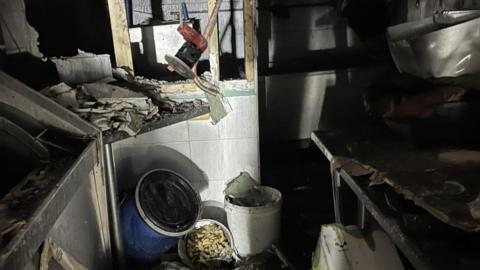 A chip shop that has been devastated in a fire. Rubble can be seen on the floor of the shop, while cabinets and the walls have been burned.