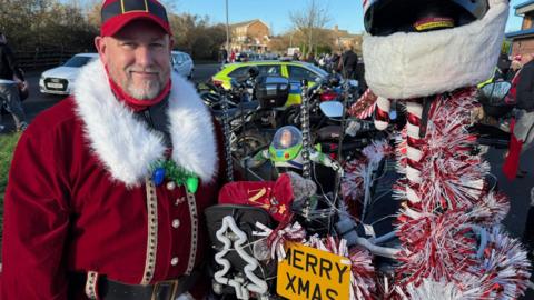 Mark Spindley is the ride organiser, he's dressed as Father Christmas and his bike has red and white tinsel on it with a Merry Xmas number plate