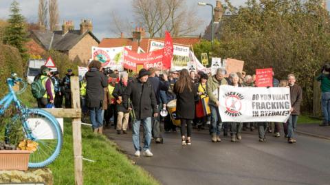 Group of people carrying banners along a road to protest against fracking