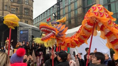 A puppet lion is paraded around Sheffield city centre. It is yellow, red and gold.