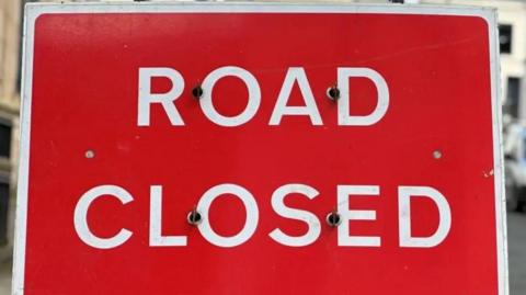 A close up of a large red sign that reads Road Closed.